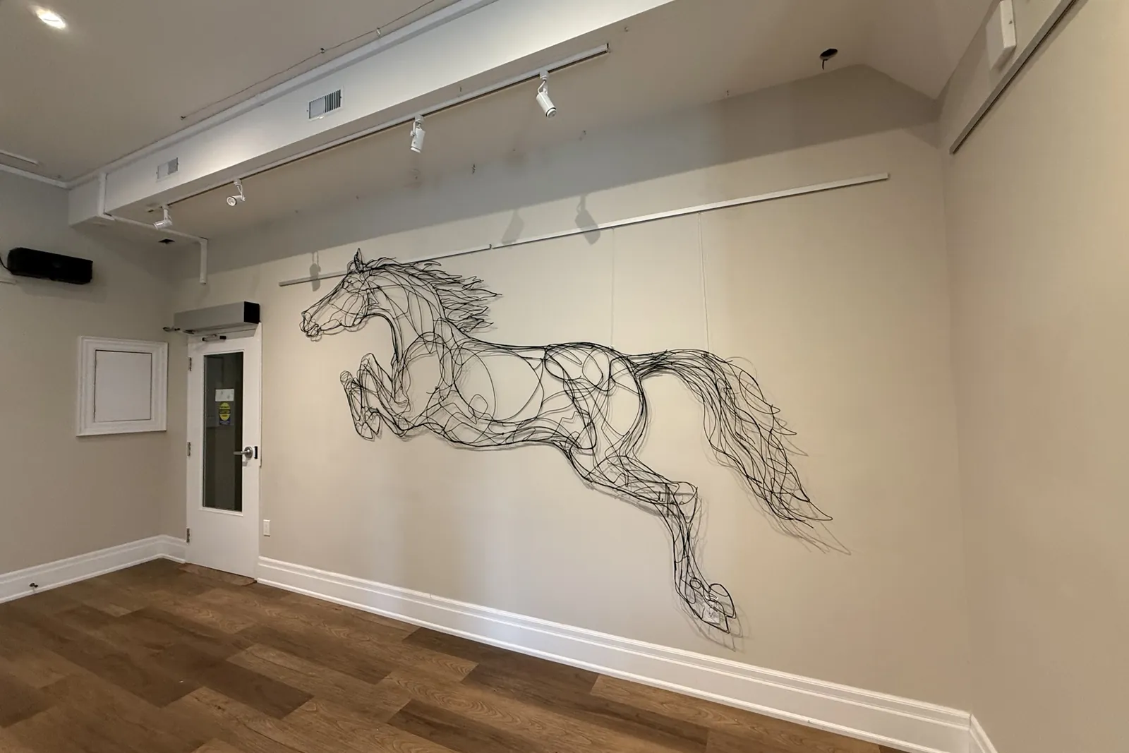 Wire sculpture of a running horse installed on a gallery wall