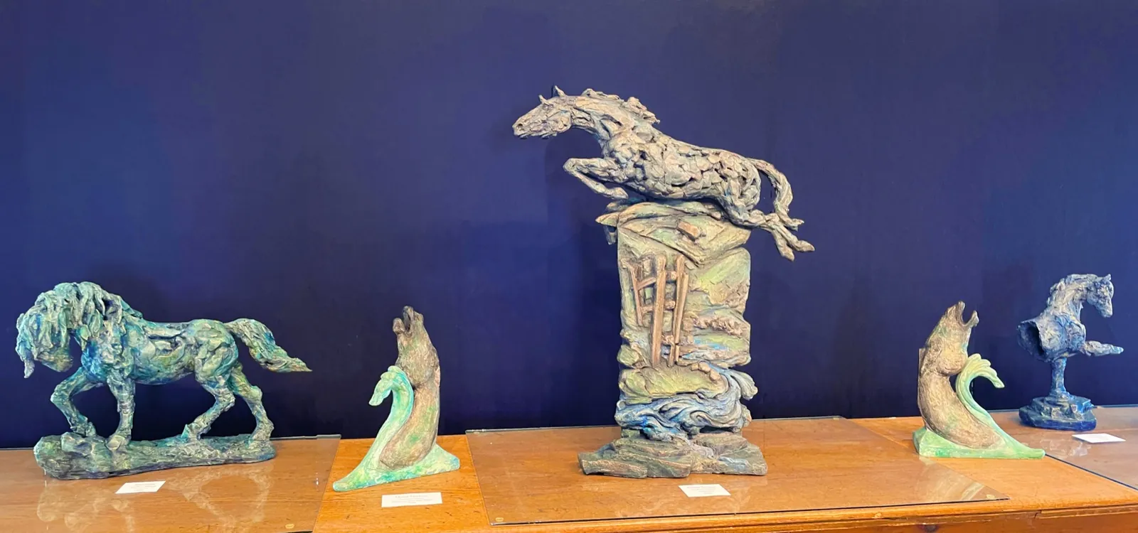 Horse sculptures displayed against a deep blue gallery wall