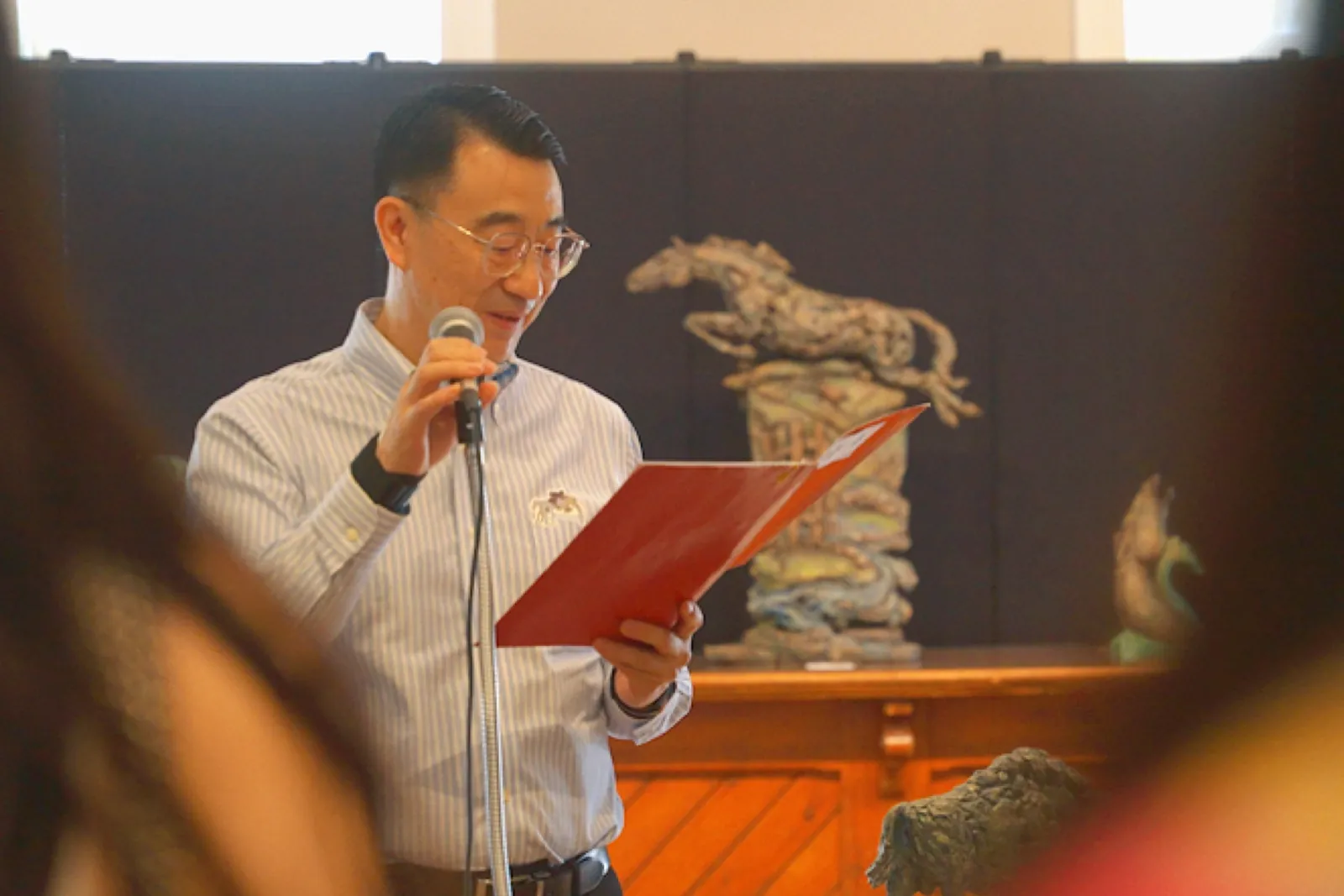 A speaker reading beside horse sculptures during the opening program