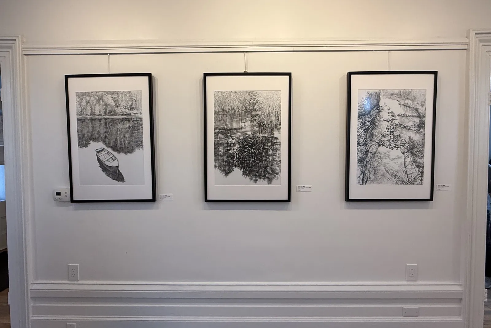 Three framed ink drawings on a gallery wall