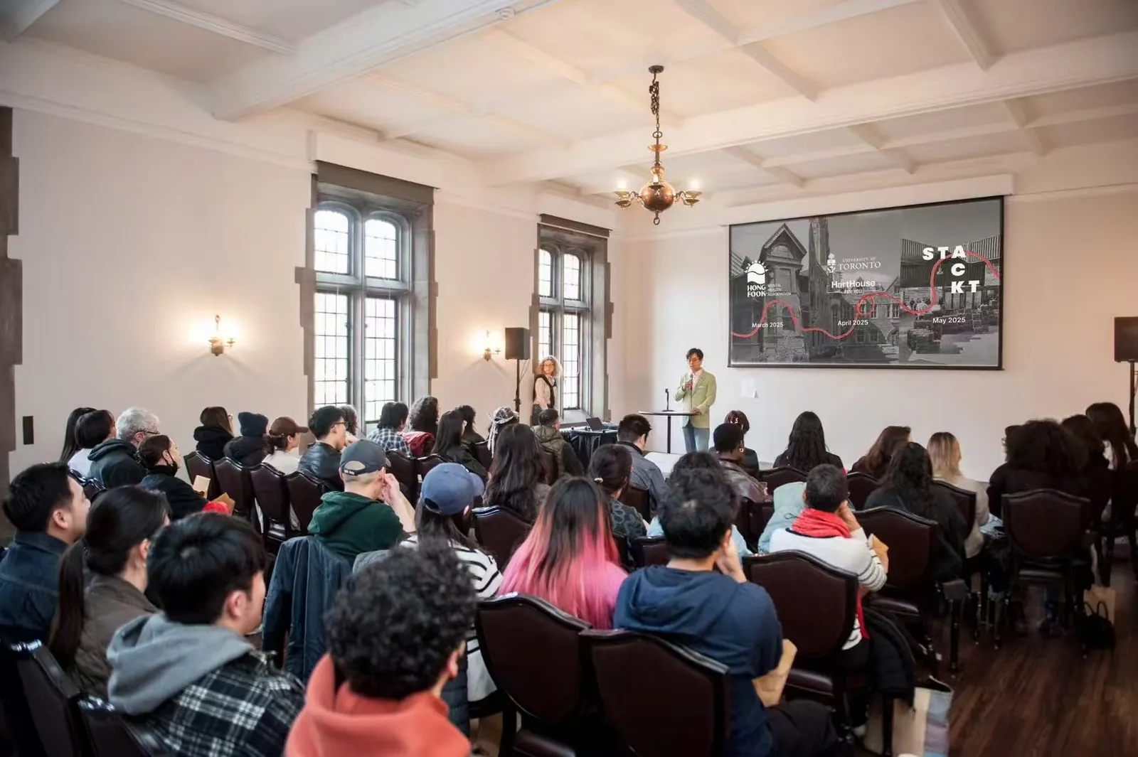 A speaker presenting to a seated audience at Hart House